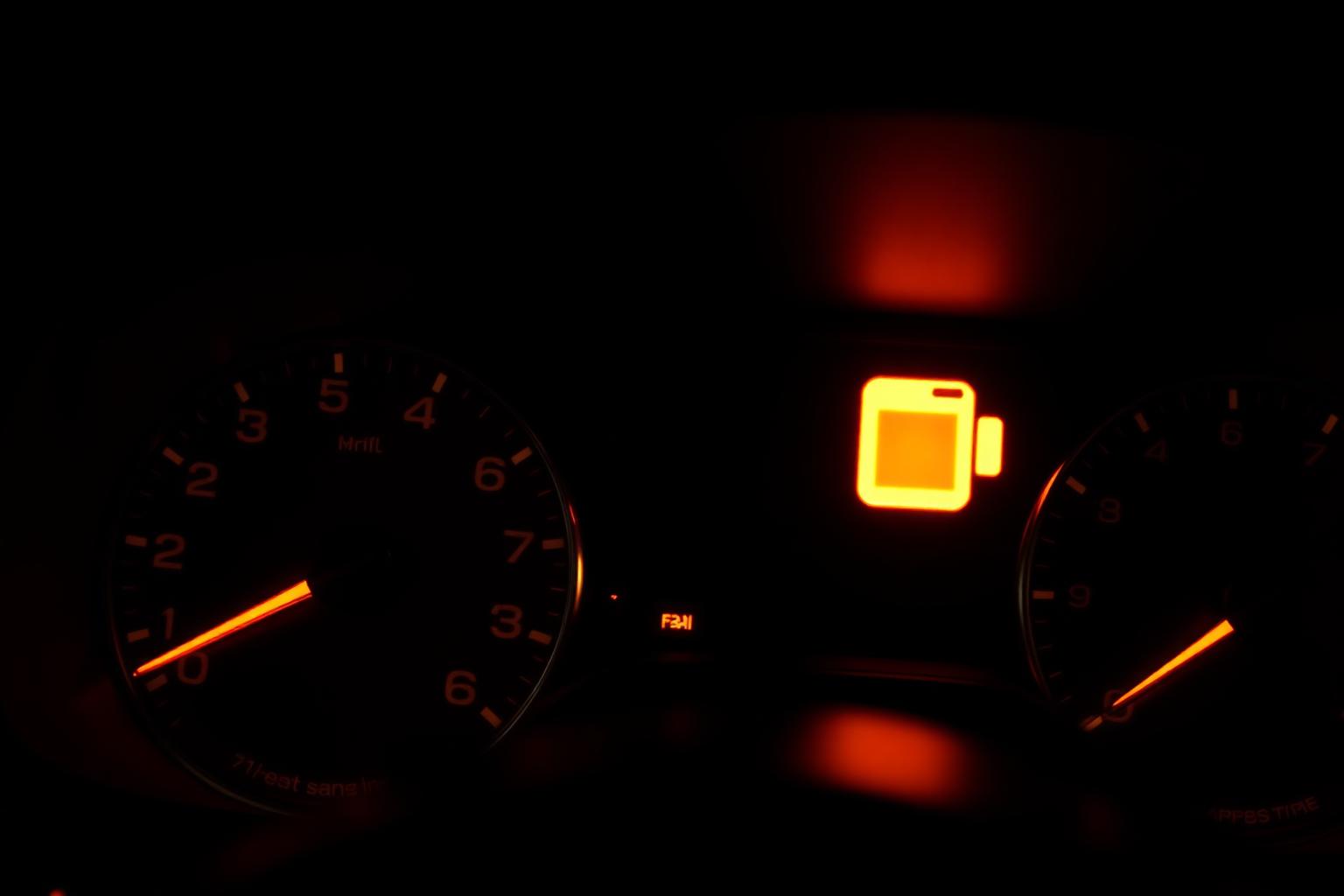 Close-up of a car dashboard with the amber check engine warning light illuminated